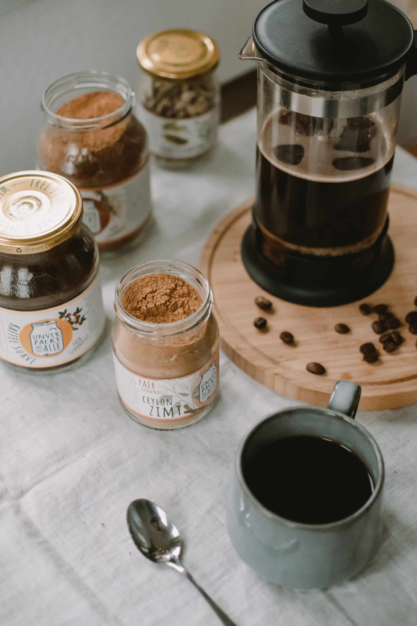 brett mit kaffee in french press und mehrweggläsern im vordergrund: zimt und Kaffee Suave